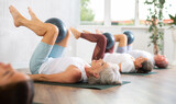 Active senior women doing pilates with soft ball lying on back in gym