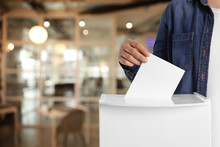 Woman Putting Her Vote Into Ballot Box On Blurred Background, Closeup