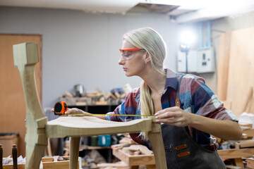 young carpenter women using measuring tape looking wood size at workspace. craftsman profession in wood factory.