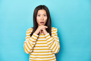Wall Mural - Asian woman in striped yellow sweater, praying for luck, amazed and opening mouth looking to front.