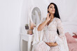 © Volodymyr - Pregnant woman strokes hugging the belly tummy abdomen enjoying pregnancy. Future family, baby infant expecting child inside, lady in white dress in bedroom modern interior