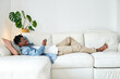© ADDICTIVE STOCK CORE - Smiling black man using smartphone and lying on cozy sofa