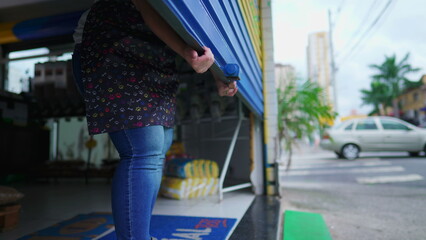 Person shutting storefront garage. Female entrepreneur closing local shop