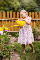 Wall Mural - a girl with a watering can watering flowers, cheerful, laughing, summer, garden, vegetable garden, village