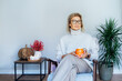 © okrasiuk - Middle aged woman relaxing with pumpkin shaped cup of hot drink in scandy style hygge interior home with fall mood decor. Lady dreaming, enjoy calm mood without stress, well being alone. Cozy autumn