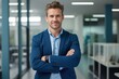 © GlobalGraphics - Happy young businessman ceo standing in office arms crossed. Smiling mature confident, professional executive manager, proud lawyer, businessman leader wearing blue suit