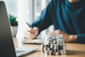 Wall Mural - businessman saving money concept. hand holding coins putting in jug glass saving money for future plan, retirement fund. Business investment-finance accounting concept.