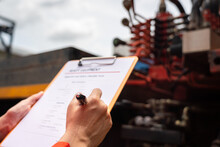 A Mechanical Engineer Is Inspecting The Condition Of Truck Crane Vehicle (as Blurred Background) Before Start The Operation On The Inspection Checklist Form. Industrial Working With Safety Practice.