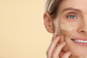 Wall Mural - Woman with swatches of foundation on face against beige background, closeup. Space for text