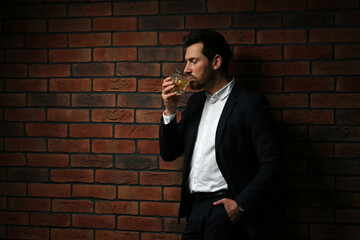 Canvas Print - Man in formal suit drinking whiskey near red brick wall. Space for text