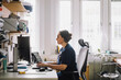 © Maskot - Side view of focused female healthcare worker using computer while sitting on desk in clinic