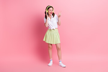 Sticker - Full length photo of carefree shiny lady wear white shirt listening music headphones showing v-sign isolated pink color background