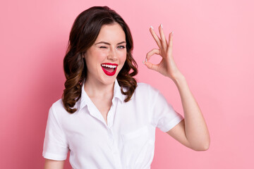 photo of good mood funky woman dressed white shirt winking showing okey gesture isolated pink color 