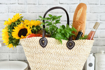 A reusable straw tote bag full of groceries from the store or market with flowers, food, wine, herbs