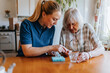 © Maskot - Female caregiver assisting senior woman while taking medicines at home