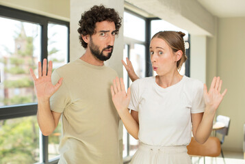 Wall Mural - young adult couple looking nervous, anxious and concerned, saying not my fault or I didn’t do it