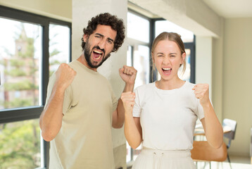 Canvas Print - young adult couple shouting aggressively with an angry expression or with fists clenched celebrating success