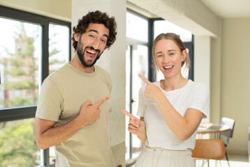 Canvas Print - young adult couple smiling cheerfully and pointing to copy space on palm on the side, showing or advertising an object