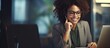 © HN Works - African American businesswoman smiles while working speaking on the phone and making notes in her office