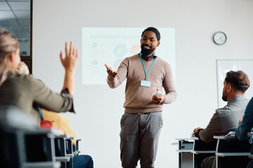 Happy black teacher pointing at student who wants to ask question during adult education training course.