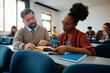 © Drazen - Black college student learning with teacher's assistance in classroom.