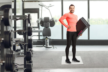 Sticker - Full length portrait of a fit young man holding a step aerobic platform at a gym