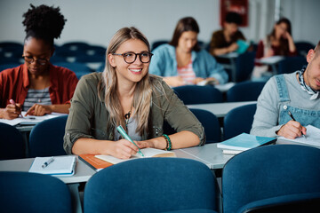 happy female student taking notes while attending lecture at university.