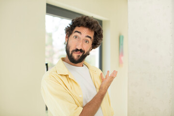 Wall Mural - young crazy bearded man feeling happy and cheerful, smiling and welcoming you, inviting you in with a friendly gesture