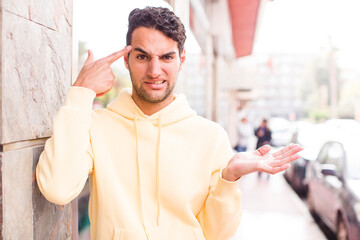 Sticker - young hispanic man feeling confused and puzzled, showing you are insane, crazy or out of your mind