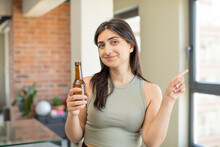 Young Woman Smiling Cheerfully, Feeling Happy And Pointing To The Side. Beer Bottle