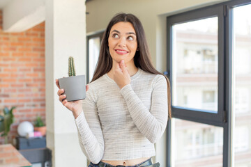 Wall Mural - pretty young model smiling with a happy, confident expression with hand on chin. decorative cactus concept