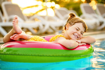 Happy little girl with inflatable toy ring float in swimming pool. Little preschool child learning to swim and dive in outdoor pool of hotel resort. Healthy sport activity and fun for children.