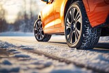 Side view of an orange car with a winter tires on a snowy road
