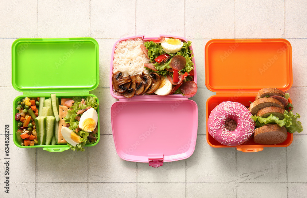 Lunchboxes with different delicious food on white tile background