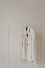 Wall Mural - White warm woolen autumn seasonal jacket on hanger over white wall. Minimalist fashion clothes wardrobe