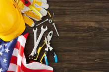 Celebrate The Invaluable Role Of Construction Workers On The American Labor Day. Top View Photo Of National Flag, Tools, Hard Hat, Gloves On Wooden Background With Empty Space For Advert Or Text