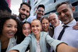 © CarlosBarquero - Selfie of happy business people taking photo with a phone. Multiracial teamwork taking a portrait of big group of colleagues. Corporative lifestyle of a diverse office workers in a financial center