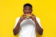 shocked african american man in white t-shirt holding big burger and surprised, amazed guy eating fast food