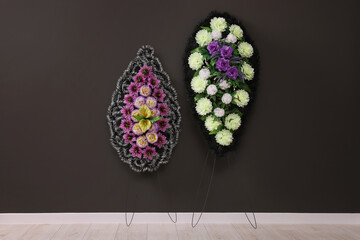 Wall Mural - Funeral wreaths of plastic flowers hanging on dark grey wall indoors