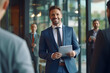 © AspctStyle - Happy young manager in a suit talking to client in front of him. Man standing inside office and talking with clients, telling colleagues good successful news.