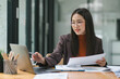 © kenchiro168 - Happy smiling business woman working with laptop computer with paperwork at desk in a modern office, business finance technology concept.