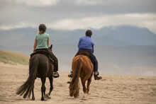 Horseback Riding On Ocean Beach. Early In The Morning Two Women Riding Together On Horses At The Sunset Beach Oregon