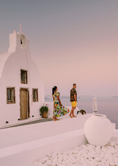 Wall Mural - Santorini Greece, young couple on luxury vacation at the Island of Santorini watching sunrise by the blue dome church and whitewashed village of Oia Santorini Greece during sunrise during summer