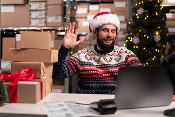 Warehouse worker talking on video call at laptop screen in storage warehouse. People working in logistic factory by virtual conference call on internet network at Christmas Eve