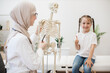 © sofiko14 - Family doctor illustrating bones to girl via skeleton model
