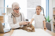 © sofiko14 - Doctor observing cat while girl distracting pet at vet's
