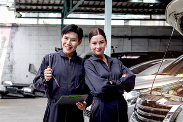 Portrait of smiling Asian mechanic man and beautiful woman in uniform standing, holding spanner at garage vehicle shop, auto mechanic technician maintenance customer car automobile at repair service.