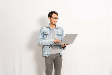 A male model uses his laptop with a happy expression. Indonesian or southeast asian model isolated with white wall background.