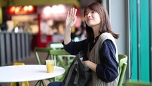 Asian-Chinese Woman Greets Smiling Looking At Camera While Waiting In A Pub Having A Soft Drink
