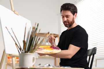 Poster - Man painting in studio. Using easel to hold canvas